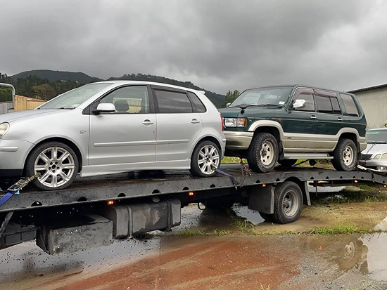 Tow truck transporting two scrap cars in Hastings.